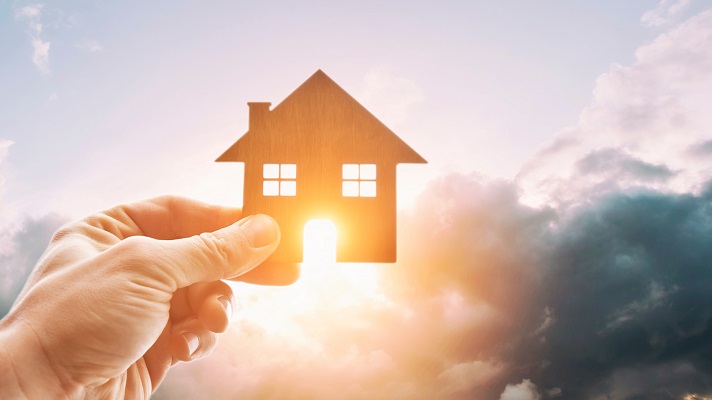 Man’s hand holds wooden flat house against the sun Energiewende im Eigenheim nur mit verlässlicher Förderung